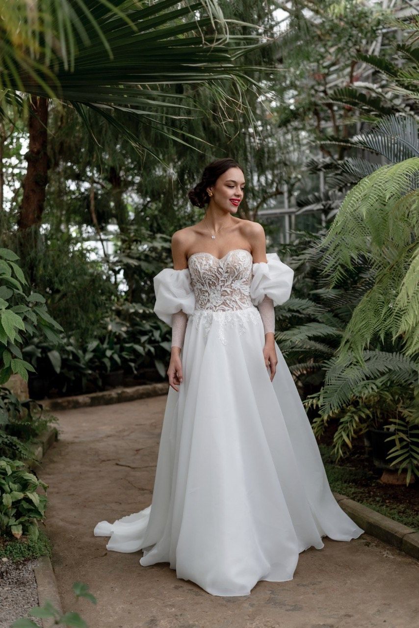 Braut mit schulterfreiem Kleid steht zwischen Bäumen