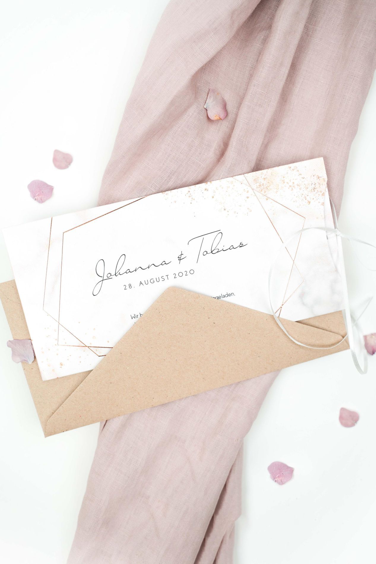 Hochzeitseinladung mit Blütenblattern und rosa Tischdecke