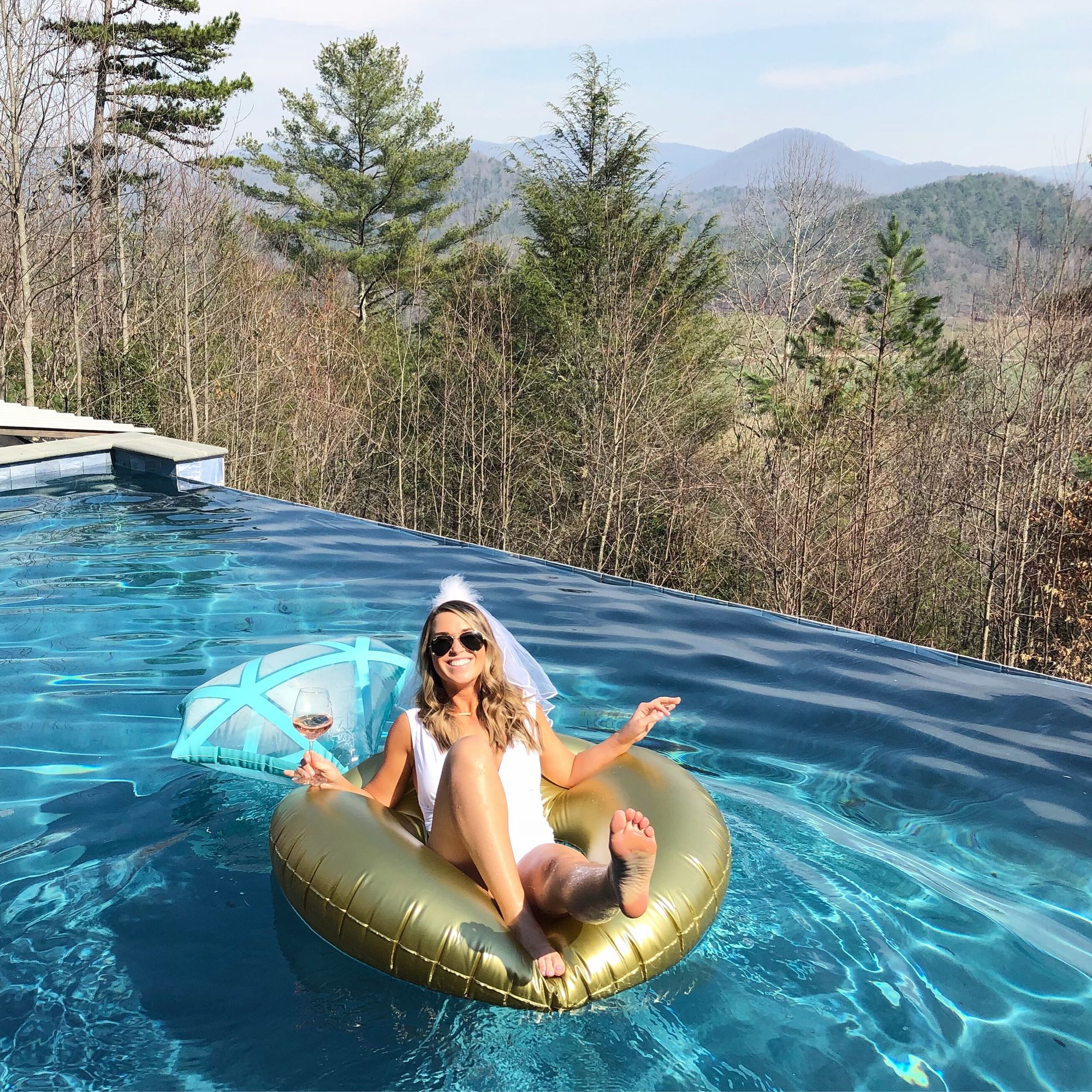 Braut auf einer Luftmatratze im Pool mit Wald im Hintergrund