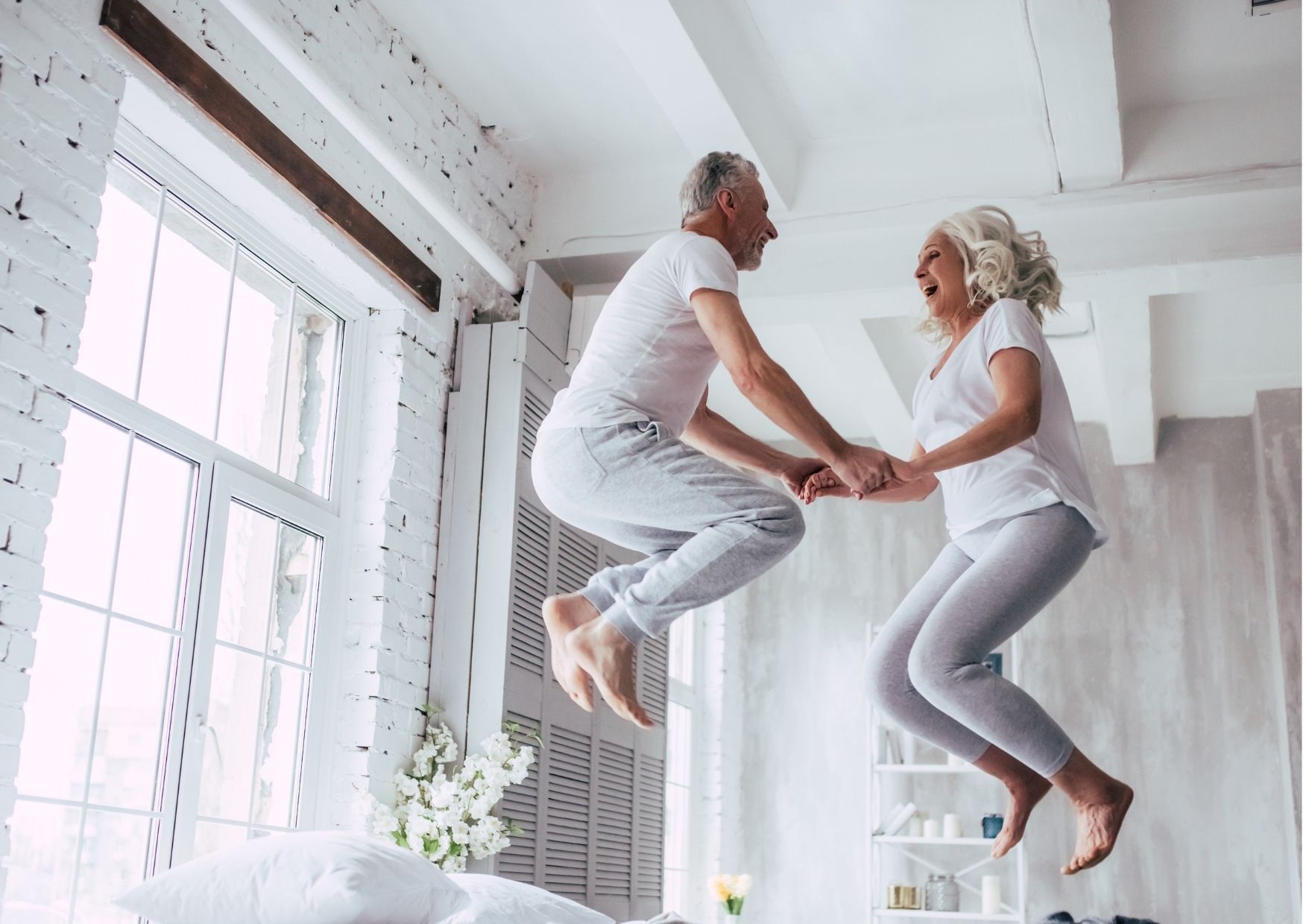Glückliches Senioren Paar springt auf dem Bett