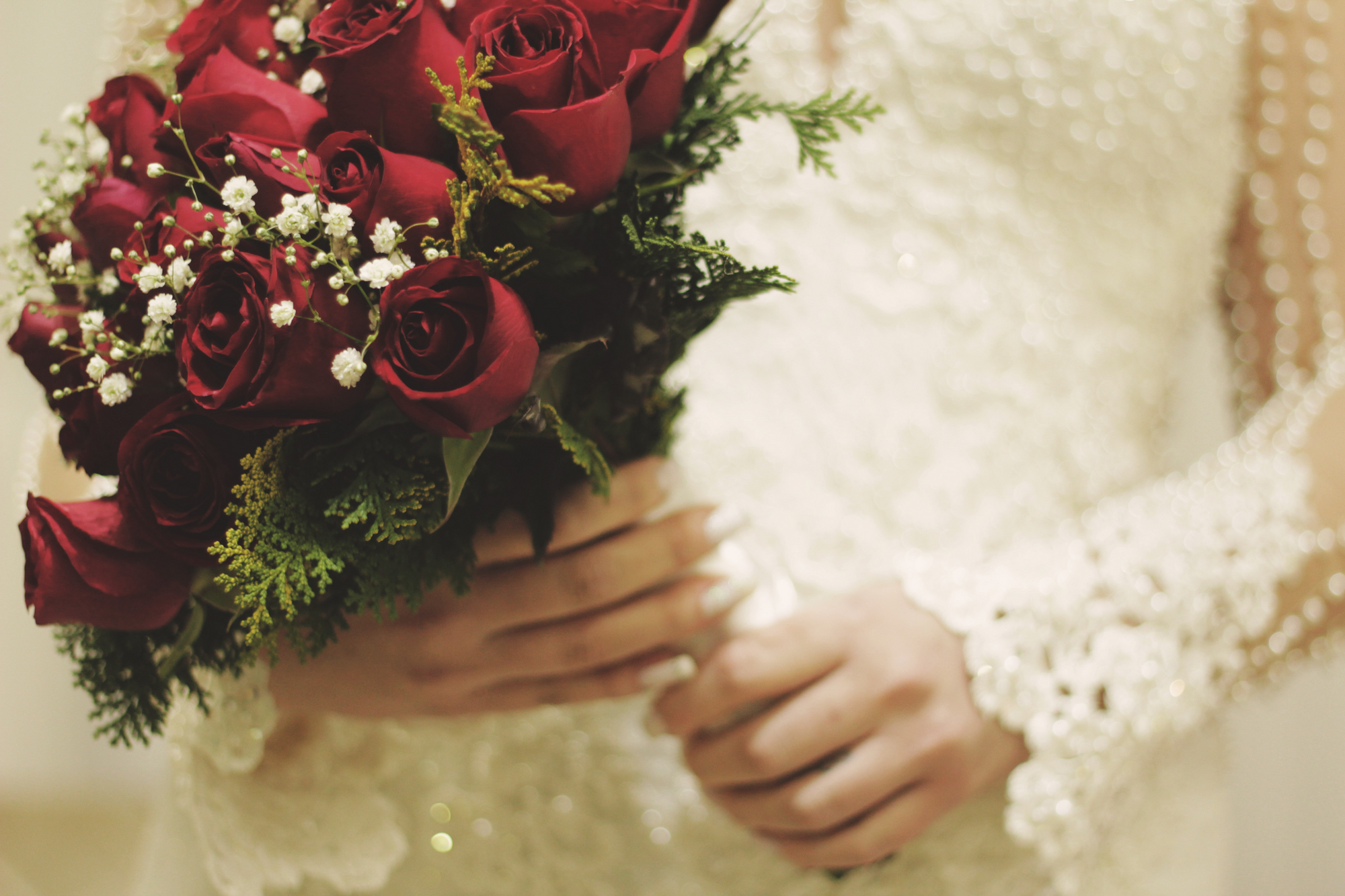 Eine Braut hält einen Brautstrauß aus roten Rosen und weißen Schleierkraut.