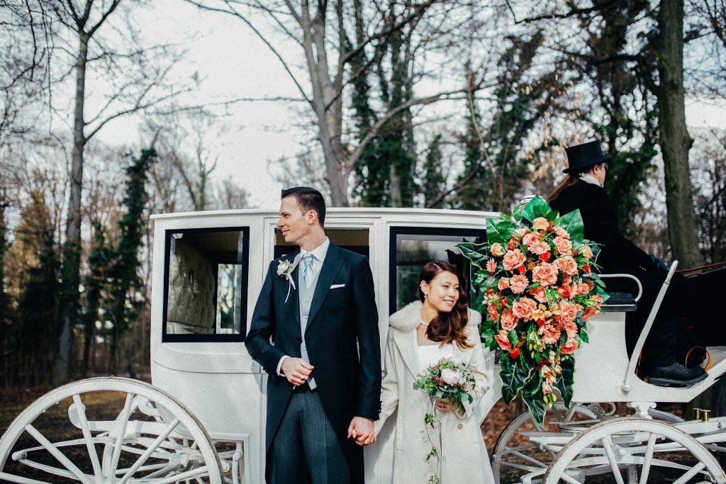 Die Braut und der Bräutigam sind gemeinsam zum Trauungsort gefahren und stehen nun zusammen vor der Hochzeitskutsche.